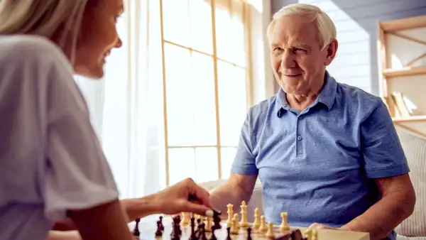 a younger caretaker playing chess with an older gentleman