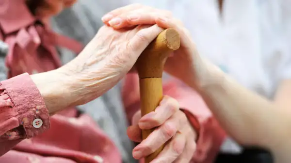 a younger caretaker with her hand on an older woman's hand while she holds a cane