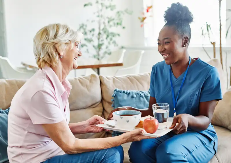 a younger caretaker holding a tray of food for an older woman