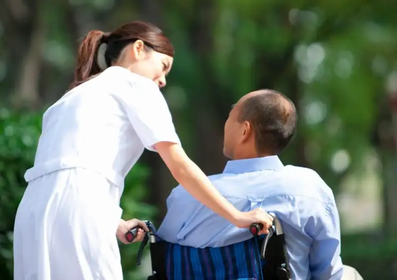 a younger caretaker pushing an older man in a wheel chair while outside